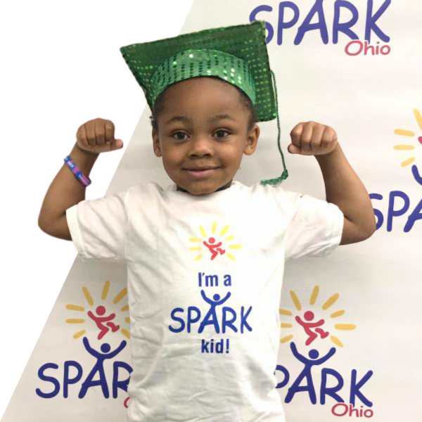 SPARK student flexing his arms with a graduation gap on
